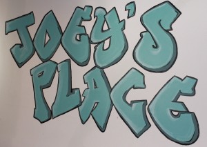 A blue graffiti featuring Joey's Place on a white surface.