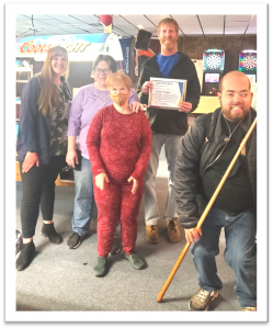 A community of people, including members of the SKSF organization, coming together in an above and beyond moment to pose for a picture at a local bowling alley.