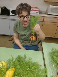 A woman, utilizing the therapeutic healing powers of gardening, sits at a table with carrots.