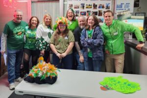 Members of SKSF's Adult Day Program posing in front of a table adorned with St. Patrick's Day decorations.