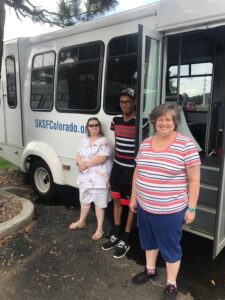 Three people with disabilities standing in front of a white bus.