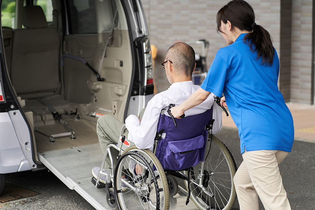 A man in a wheelchair receiving support as he is empowered while being helped out of a van.