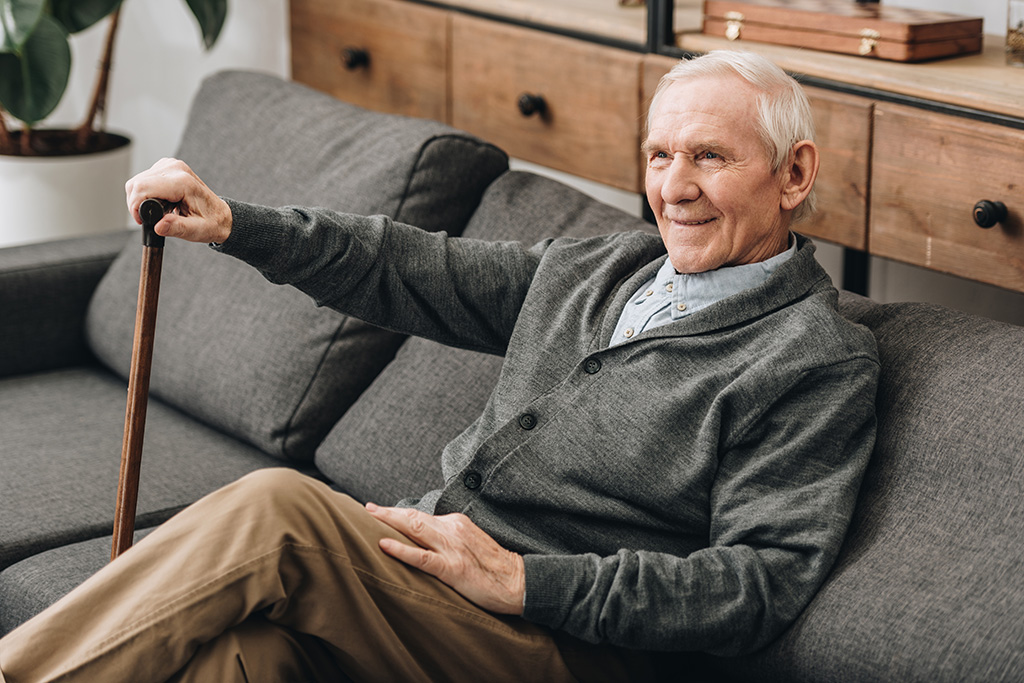 An elderly man sitting on a residential couch with a cane.