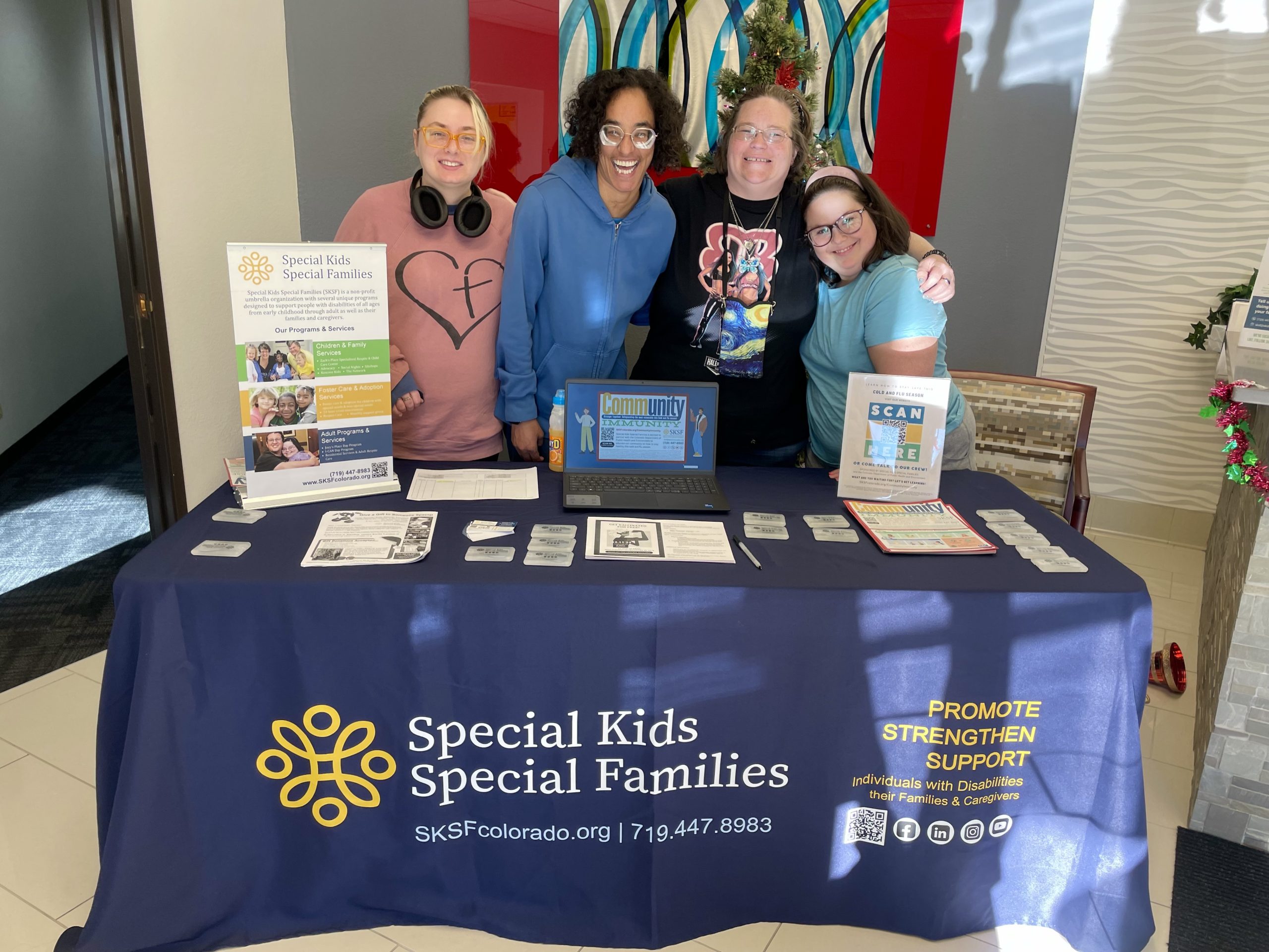 CommunityImmunity(2) Four people stand behind an informational table for Special Kids Special Families, featuring brochures, pamphlets, and a promotional tablecloth.