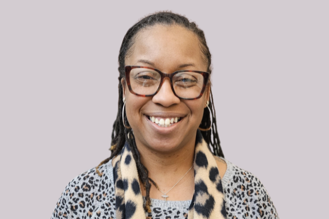 Person with glasses and a leopard-print scarf smiles at the camera against a plain light gray background.
